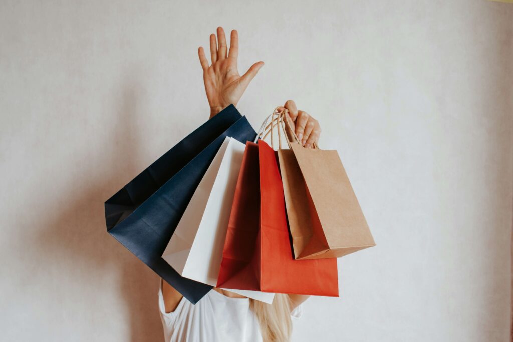 複数のショッピングバッグを掲げる女性。買い物の習慣を見直すイメージ